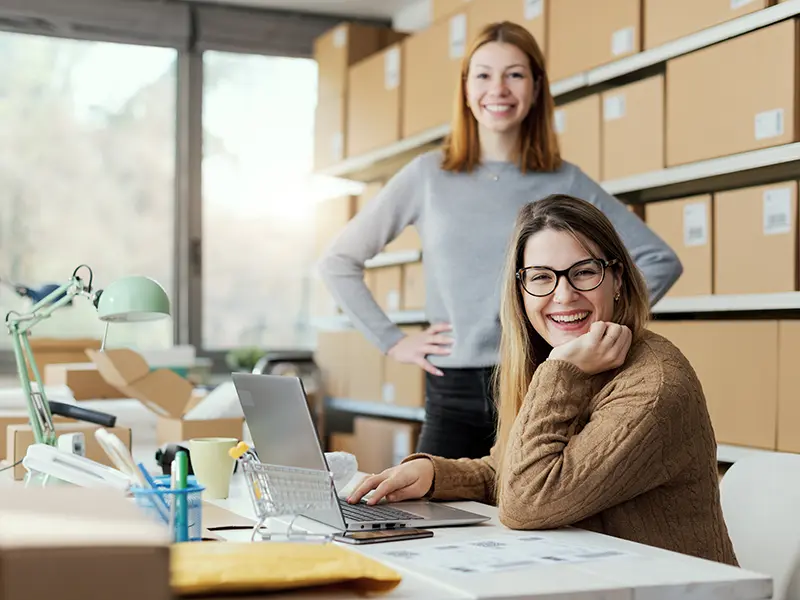 two smiling woman in office with lapt op